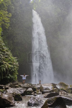 Foto de Joven madre de familia con los viajeros hija explorar cascada en la selva de Bali, concepto de viaje, vacaciones en Asia. - Imagen libre de derechos