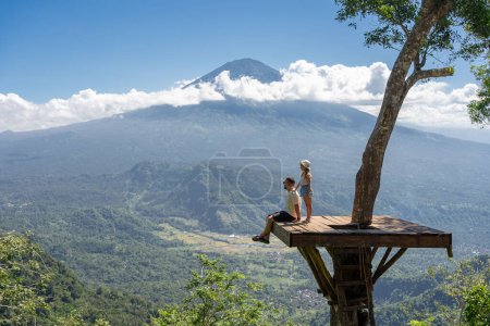 Photo for Father and daughter tourists enjoying travel around Bali island , Indonesia. They stands on photo location on the tree with view on Agung Mountain - Royalty Free Image