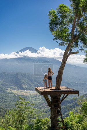 Photo for Mother and daughter tourists enjoying travel around Bali island , Indonesia. They stands on photo location on the tree with view on Agung Mountain - Royalty Free Image