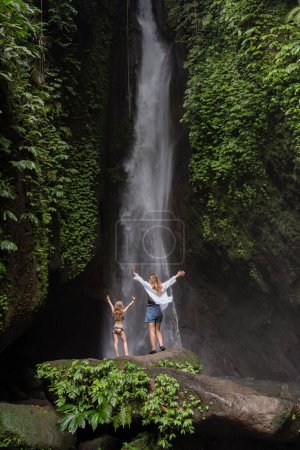 Photo for Family at a tropical waterfall. A woman and child at a beautiful waterfall. Vacation on a tropical island. Traveling couple at the waterfall. Family on vacation in Bali - Royalty Free Image