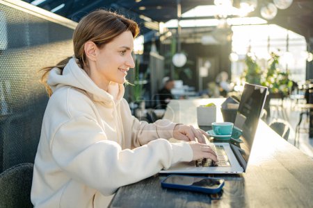 Téléchargez les photos : Femme caucasienne se connectant à Internet sans fil 4g sur ordinateur netbook moderne, Jeune fille hipster travaillant sur ordinateur portable dans un café - en image libre de droit