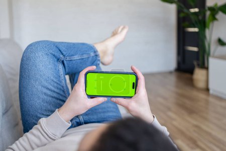 Foto de Hombre en casa Descansando en un sofá usando Smartphone con Green Mock-up Screen. Guy Usando Teléfono Móvil, Internet Redes Sociales Navegación - Imagen libre de derechos