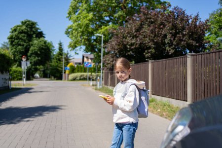 Téléchargez les photos : L'enfant regarde un téléphone cellulaire en traversant une route devant la voiture. Concept de dépendance au téléphone portable. - en image libre de droit