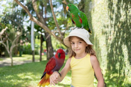 Téléchargez les photos : Enfant fille avec beau perroquet aras dans son épaule dans le zoo, Bali, Indonésie. - en image libre de droit