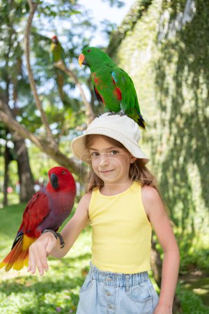 Photo for Child girl with beautiful macaw parrot in her shoulder in the zoo, Bali, Indonesia. - Royalty Free Image
