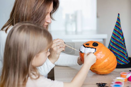 Photo for Little girl making Halloween decoration with parent at home, drawing scary face on pumpkin and enjoying holiday preparation - Royalty Free Image