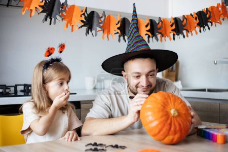 Téléchargez les photos : Père et fille faisant des décorations d'Halloween à la maison, se préparant pour la fête - en image libre de droit