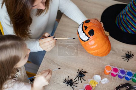 Photo for Mother and little daughter decorate Halloween pumpkin at home. - Royalty Free Image