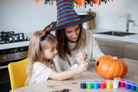 Foto de Madre e hija pequeña decoran la calabaza de Halloween en casa. - Imagen libre de derechos
