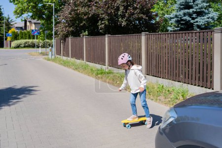 Photo for Accident. Small girl on the skateboard crosses the road in front of a car. - Royalty Free Image