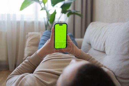 Foto de Primer plano de la persona que se relaja en el sofá y el uso de un teléfono inteligente con pantalla verde simulada. Hombre sosteniendo una pantalla verde smartphone - Imagen libre de derechos