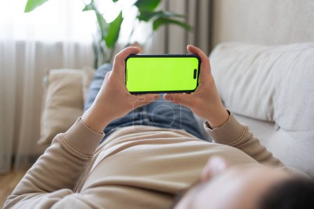 Foto de Primer plano de la persona que se relaja en el sofá y el uso de un teléfono inteligente con pantalla verde simulada. Hombre sosteniendo una pantalla verde smartphone - Imagen libre de derechos
