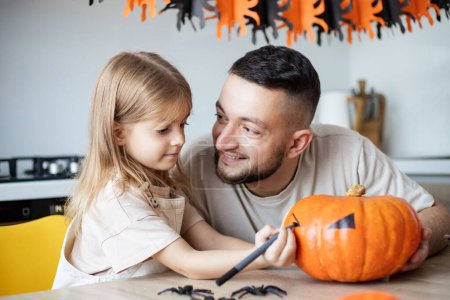 Photo for Father and daughter making Halloween decorations at home while sitting at wooden table - Royalty Free Image
