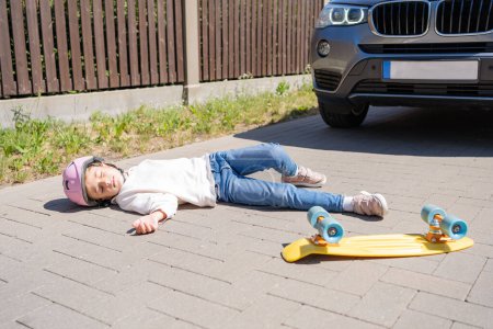 Téléchargez les photos : Fille sur le skateboard a été frappé par la voiture. Le concept d'accidents de la route et la réduction des accidents dus à l'utilisation de voitures sur la route. - en image libre de droit