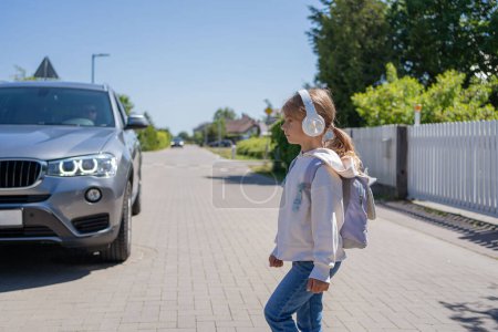 Photo for Girl with headphones and cellphone crossing the road, not looking at car let - Royalty Free Image