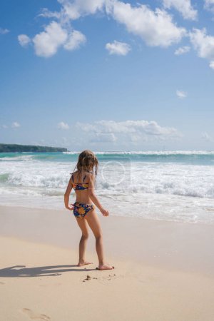 Foto de Niña sonriente corriendo y jugando en la playa mientras está de vacaciones en familia. Jugar en las olas del océano divertirse y ser activo. - Imagen libre de derechos
