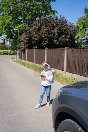 Photo for Girl with headphones and cellphone crossing the road, not looking at car - Royalty Free Image
