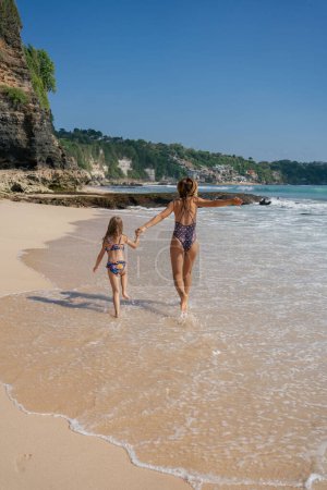 Téléchargez les photos : Belle petite fille jouissant avec sa mère sur la plage. Ils courent au bord de la mer et s'amusent. Photo de haute qualité - en image libre de droit