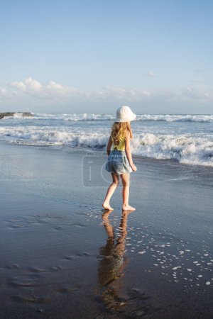 Téléchargez les photos : Amusez-vous sur la plage de la mer tropicale à Bali. Funny girl courir avec des éclaboussures par la piscine d'eau le long du bord de surf. Mode de vie actif des enfants. - en image libre de droit