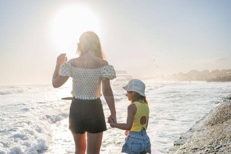 Foto de Madre con hija mira las olas en un día soleado - Imagen libre de derechos