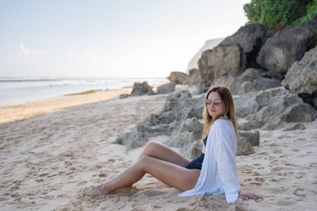 Photo for Young woman sitting on the beach alone, relax and enjoy nature - Royalty Free Image