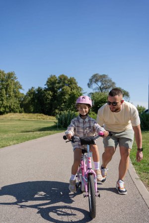 Photo for Father teaching daughter to ride bike in park - Royalty Free Image