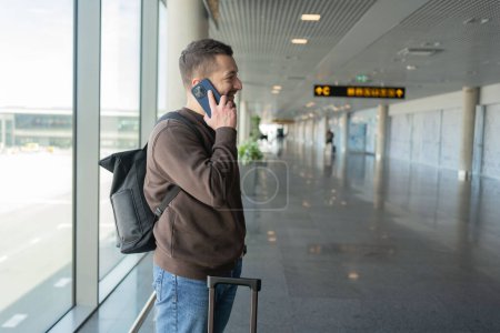 Photo for Portrait of man talking on cellphone in airport, Guy enjoying phone conversation while waiting for flight in terminal. - Royalty Free Image