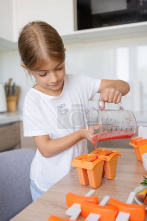 Photo for The process of making ice cream. Child making tasty ice lollipops in moulds on countertop in kitchen during free time. - Royalty Free Image