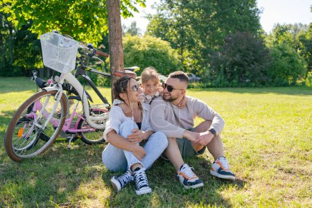 Photo for Family with child after cycling trip, sitting on grass and resting, have fun and enjoy time together - Royalty Free Image