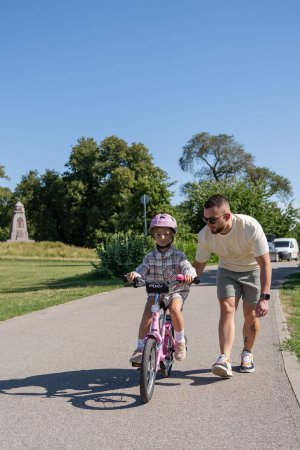 Foto de Padre enseñando a la hija a montar en bicicleta en el parque - Imagen libre de derechos