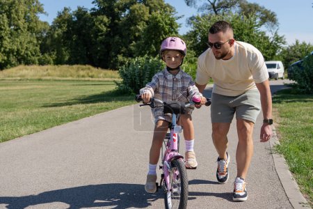 Téléchargez les photos : Père enseignant la fille à faire du vélo dans le parc - en image libre de droit