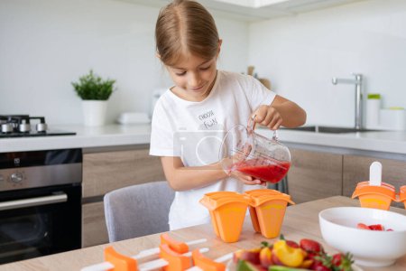 Téléchargez les photos : Le processus de fabrication de crème glacée. Enfant faisant sucettes de glace savoureuses dans les moules sur le comptoir dans la cuisine pendant le temps libre. - en image libre de droit