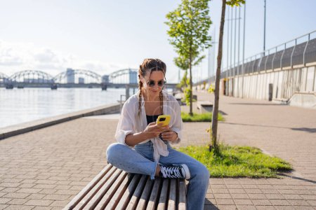 Foto de Mujer joven hipster sentado en la calle de la ciudad, el uso de celofán, charlando con amigos, tienen videollamada - Imagen libre de derechos