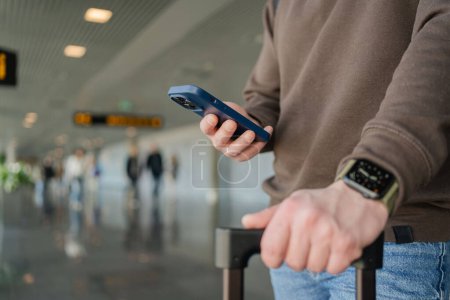 Téléchargez les photos : Un touriste occupé dans la salle d'attente. Jeune homme avec téléphone portable à l'aéroport en attendant l'avion - en image libre de droit