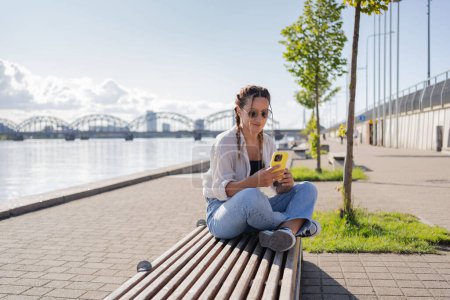 Foto de Mujer joven hipster sentado en la calle de la ciudad, el uso de celofán, charlando con amigos, tienen videollamada - Imagen libre de derechos
