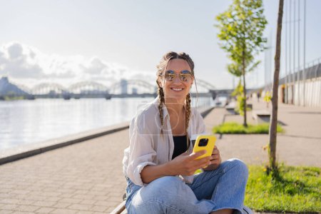 Téléchargez les photos : Jeune femme hipster assis dans la rue de la ville, utiliser la cellophane, bavarder avec des amis, avoir un appel vidéo - en image libre de droit