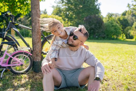 Photo for Laughing father and his daughter having fun together at the green park, relax and have fun together after cycling . - Royalty Free Image