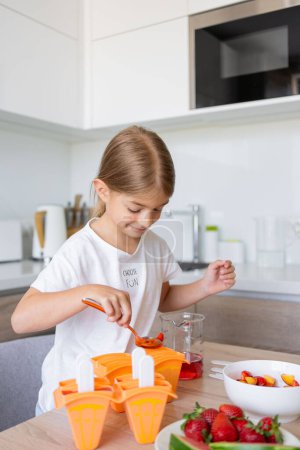 Téléchargez les photos : Le processus de fabrication de crème glacée. Enfant faisant sucettes de glace savoureuses dans les moules sur le comptoir dans la cuisine pendant le temps libre. - en image libre de droit