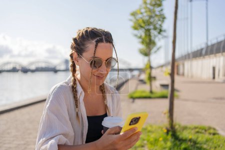 Téléchargez les photos : Jeune femme hipster assis dans la rue de la ville, utiliser la cellophane, bavarder avec des amis, avoir un appel vidéo - en image libre de droit
