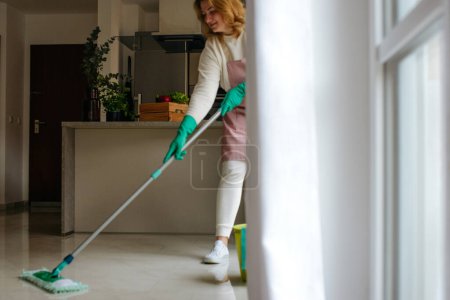 Téléchargez les photos : Jeune femme avec seau de nettoyage et balai prêt à commencer à essuyer le sol de la cuisine, à l'intérieur. La femme de ménage fait le ménage - en image libre de droit