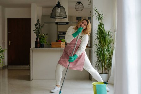 Foto de Mujer feliz limpiando la casa, cantando en el micrófono y divirtiéndose, espacio libre. Ama de casa disfruta de las tareas domésticas mientras que la limpieza creativa de la casa - Imagen libre de derechos