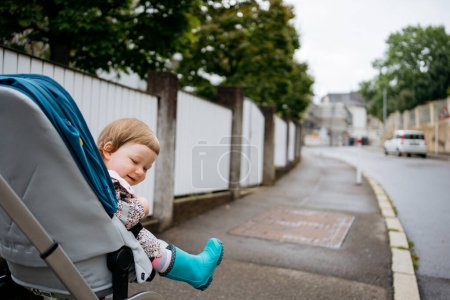 Photo for A happy little girl sits in a pram driving down the street - Royalty Free Image