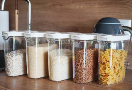 Foto de Diferentes tipos de cereales y pastas en recipientes en una mesa de madera de cocina - Imagen libre de derechos