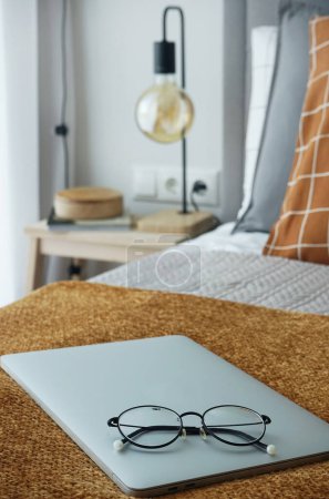 Foto de Una mesa de madera con una lámpara y decoración junto a la ventana y una cama con ropa de cama a cuadros, una tela a cuadros marrón, un ordenador portátil y vasos - Imagen libre de derechos
