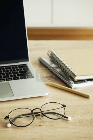 Foto de Un portátil abierto, cuadernos, un bolígrafo y vasos se encuentran sobre una mesa de madera - Imagen libre de derechos