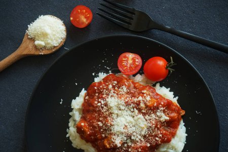 Foto de Arroz con salsa de tomate, albóndigas y parmesano en un plato negro junto a un tenedor y tomates cherry sobre un mantel gris - Imagen libre de derechos