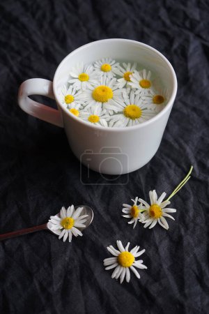 Foto de Taza con flores de té y margarita sobre un fondo oscuro - Imagen libre de derechos