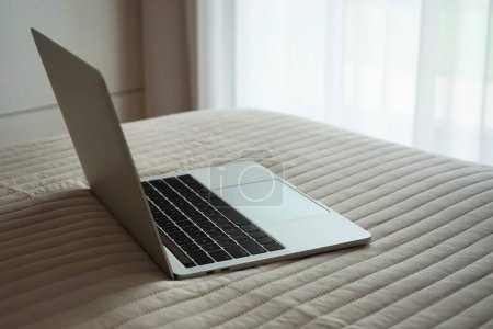 Foto de Un portátil gris abierto yace sobre una manta en un dormitorio luminoso - Imagen libre de derechos