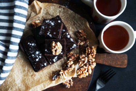 Foto de Pastel de chocolate con nueces en una tabla de madera junto a tazas de té sobre un fondo oscuro - Imagen libre de derechos