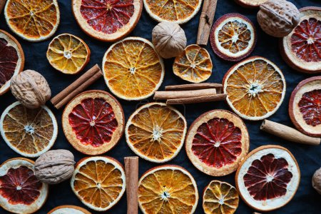 Photo for Dry orange and grapefruit slices next to cinnamon and walnuts on a dark background - Royalty Free Image